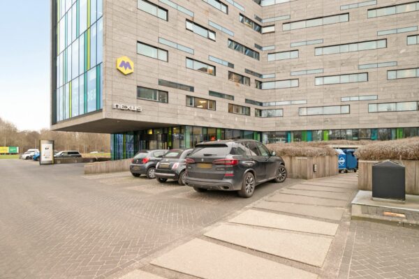 Ingang en parkeerplaats van het kantoorgebouw Nexus aan de Zwartewaterallee 56 met geparkeerde auto's op de voorgrond.