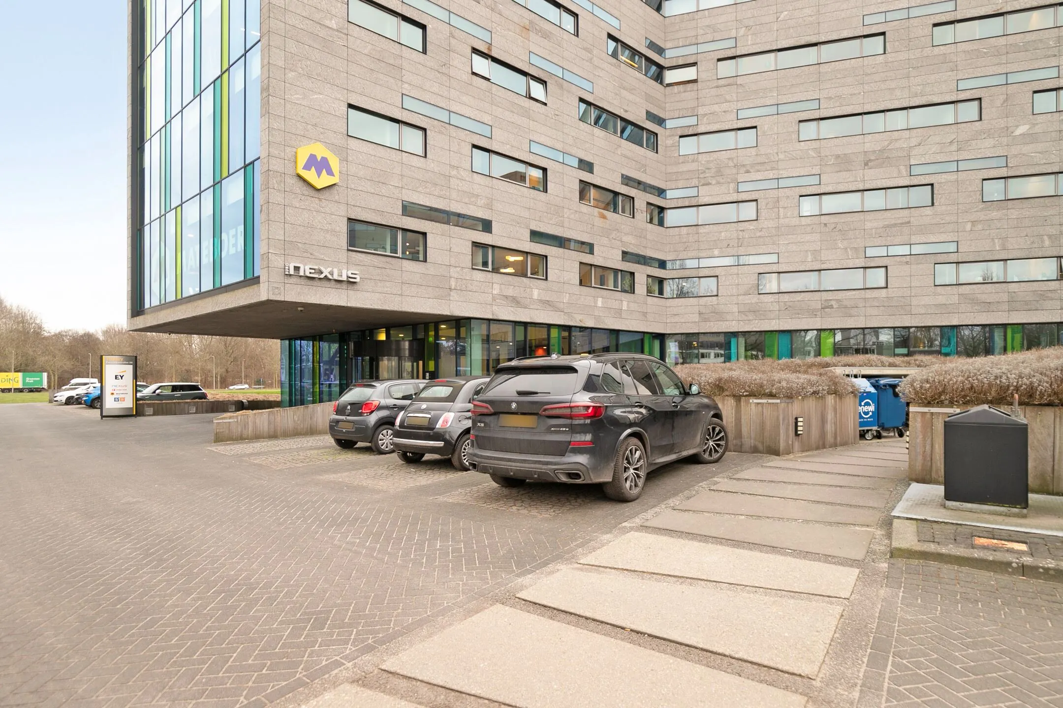 Ingang en parkeerplaats van het kantoorgebouw Nexus aan de Zwartewaterallee 56 met geparkeerde auto's op de voorgrond.