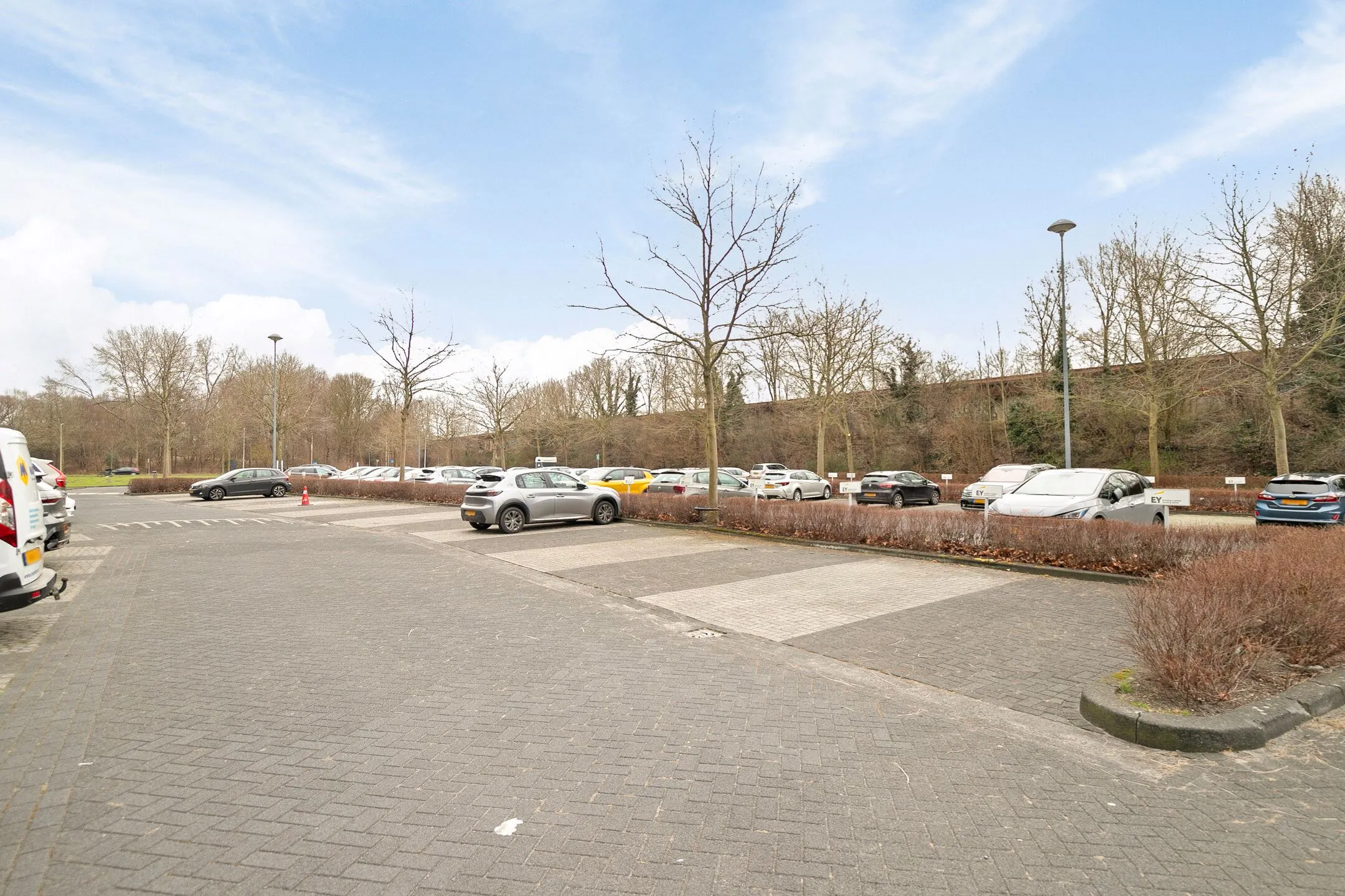 Parkeerterrein met geparkeerde auto's en kale bomen bij Zwartewaterallee 56.