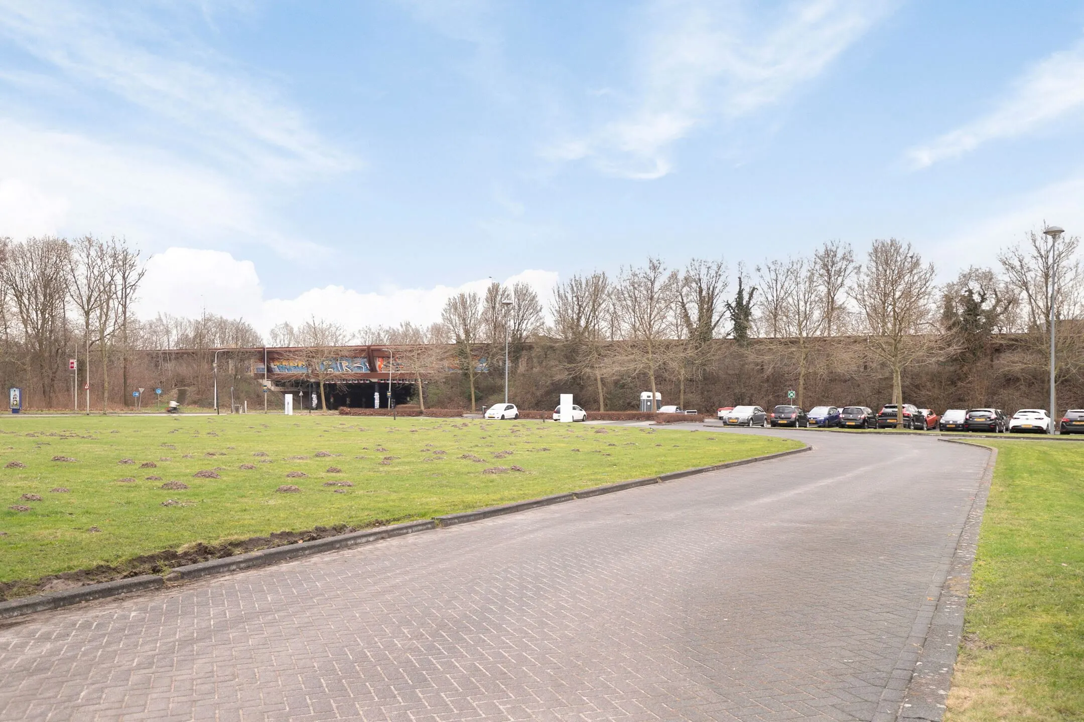 Parkeerplaats aan de Zwartewaterallee met geparkeerde auto's en een viaduct op de achtergrond.