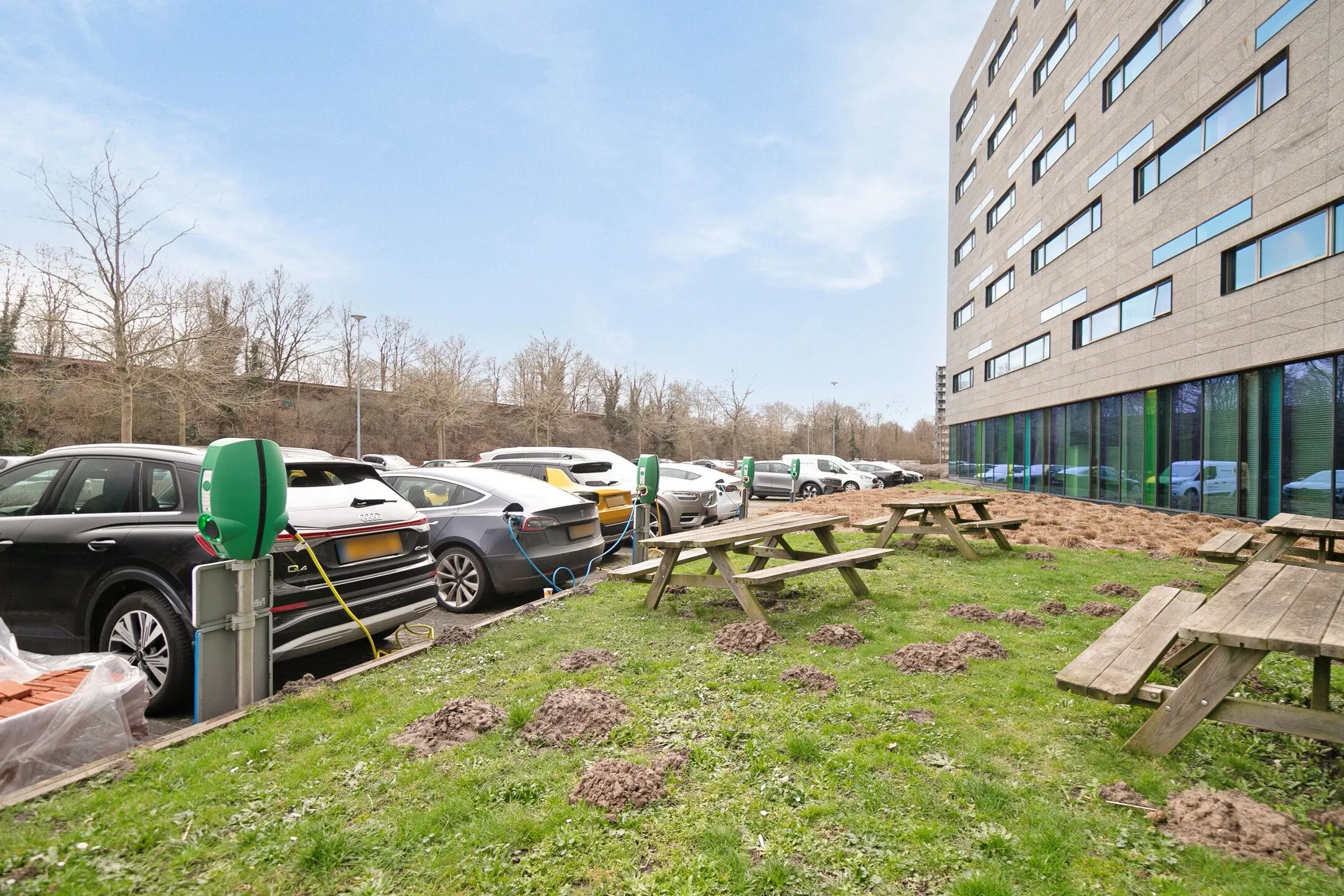 Parkeerplaats met laadpalen en elektrische auto's naast een kantoorgebouw aan de Zwartewaterallee, met picknicktafels op een grasveld op de voorgrond.