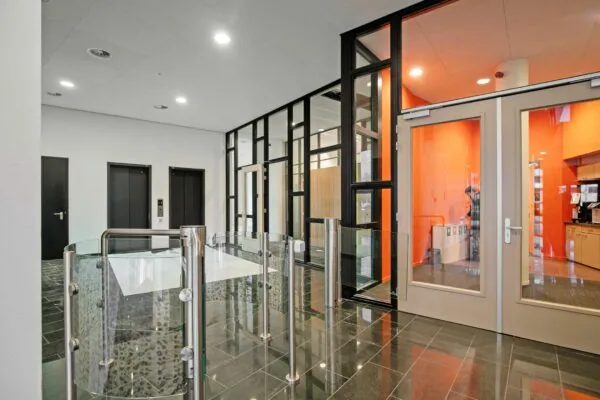 Ingangsgebied van het kantoorgebouw aan de Zwartewaterallee 56 met glazen toegangspoortjes, liften en een feloranje wand in de achtergrond.