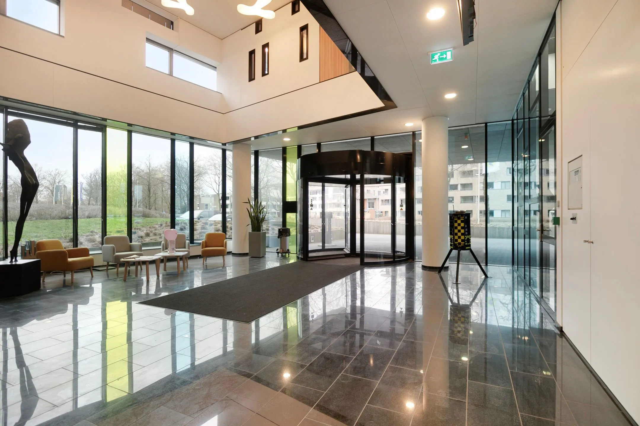 Moderne en ruime ontvangsthal van Zwartewaterallee 56 met glazen draaideur, zitgedeelte en kunstwerk.