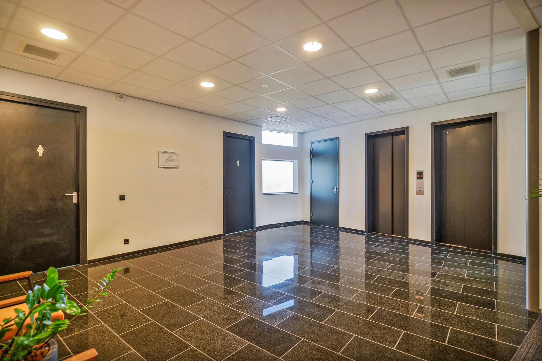 Modern ingerichte hal op Zwartewaterallee 56 met zwarte deuren, twee liften en glanzende zwarte tegelvloer.