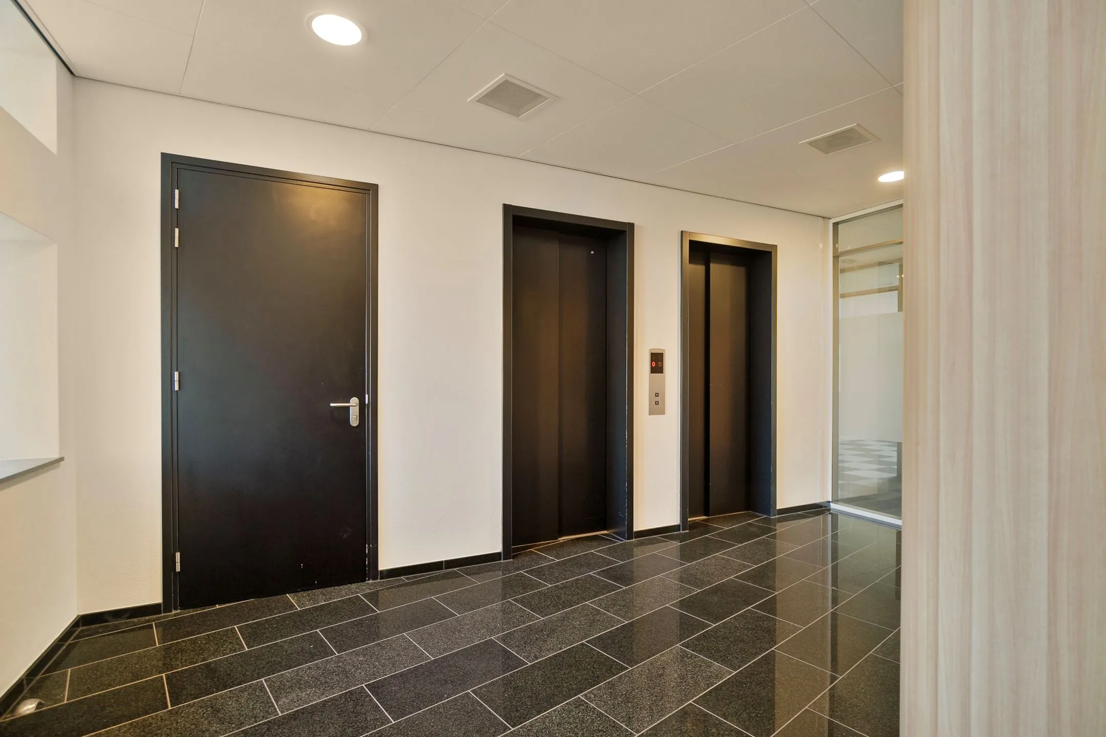 Moderne entree met twee liften en een zwarte deur in het kantoorgebouw aan de Zwartewaterallee 56.