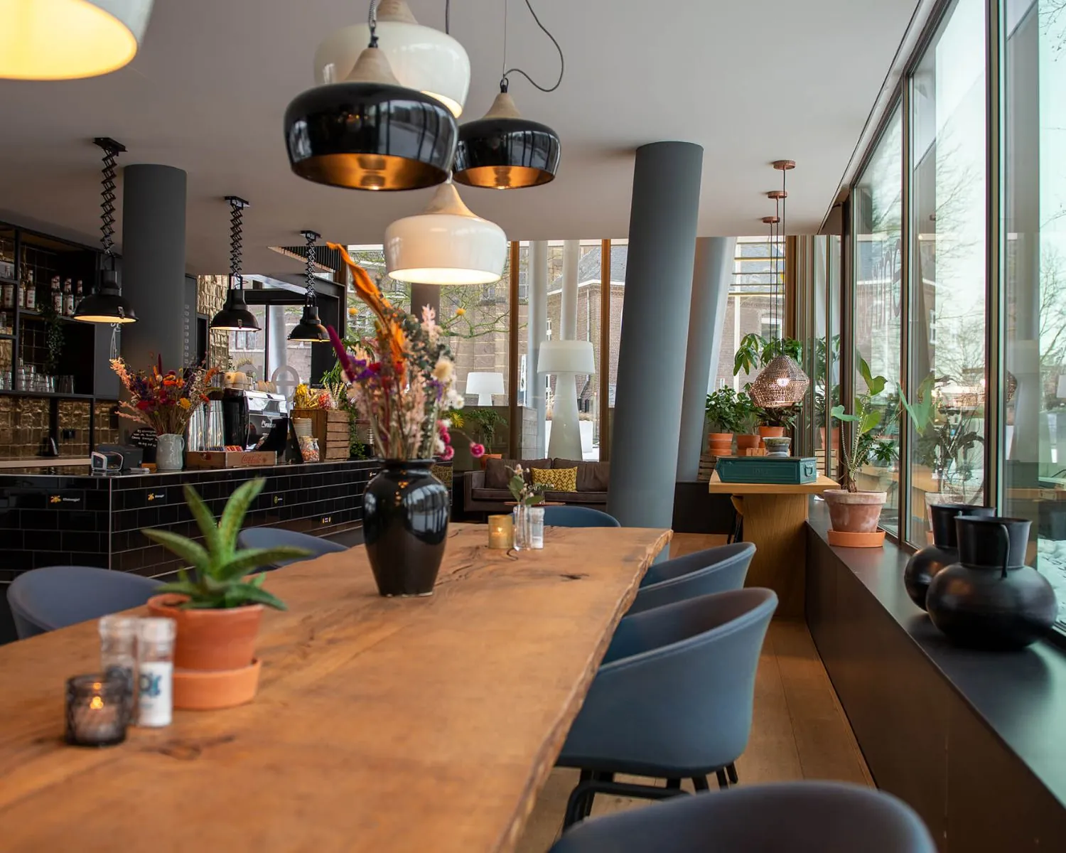 Modern ingericht café in Zwolle met een houten lange eettafel, stijlvolle verlichting en veel planten.