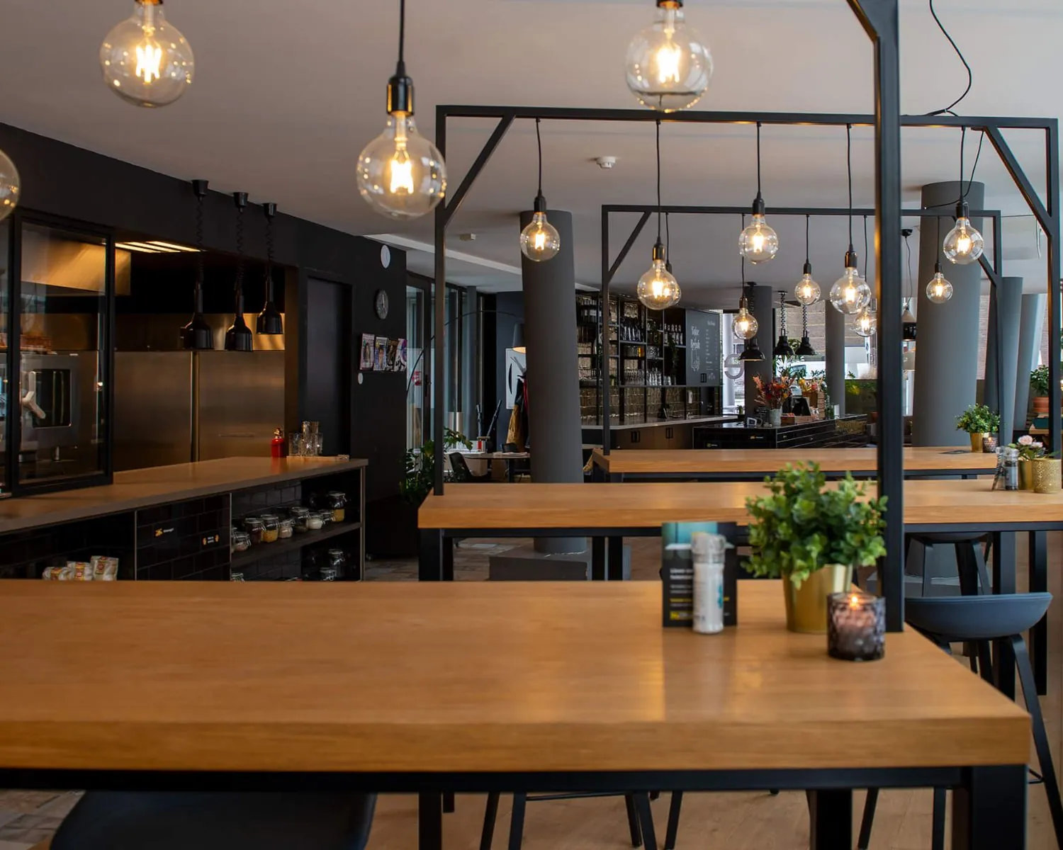 Modern interieur van een restaurant in Zwolle met houten tafels, hanglampen en een open keuken.