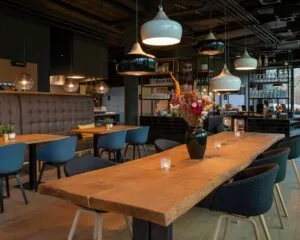 Modern restaurantinterieur in Zwolle met houten tafels, designverlichting en een centraal geplaatste bloemenvaas.