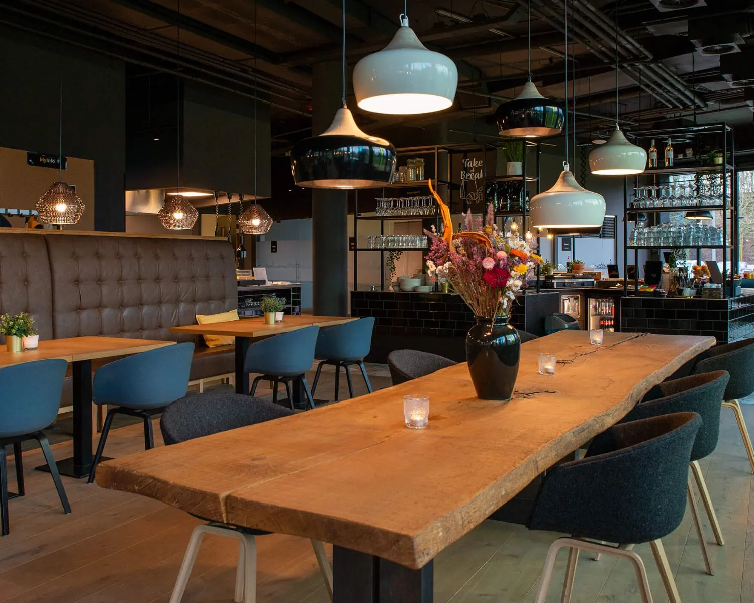 Modern restaurantinterieur in Zwolle met houten tafels, designverlichting en een centraal geplaatste bloemenvaas.