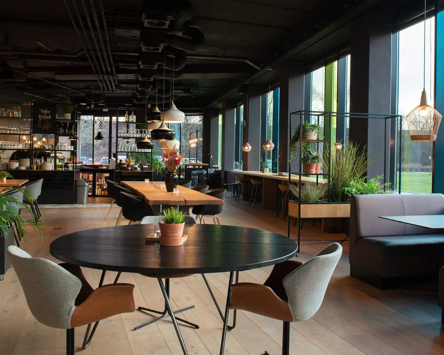 Modern ingericht restaurant aan de A28 bij Zwolle met houten vloeren, zwarte tafels en veel planten.