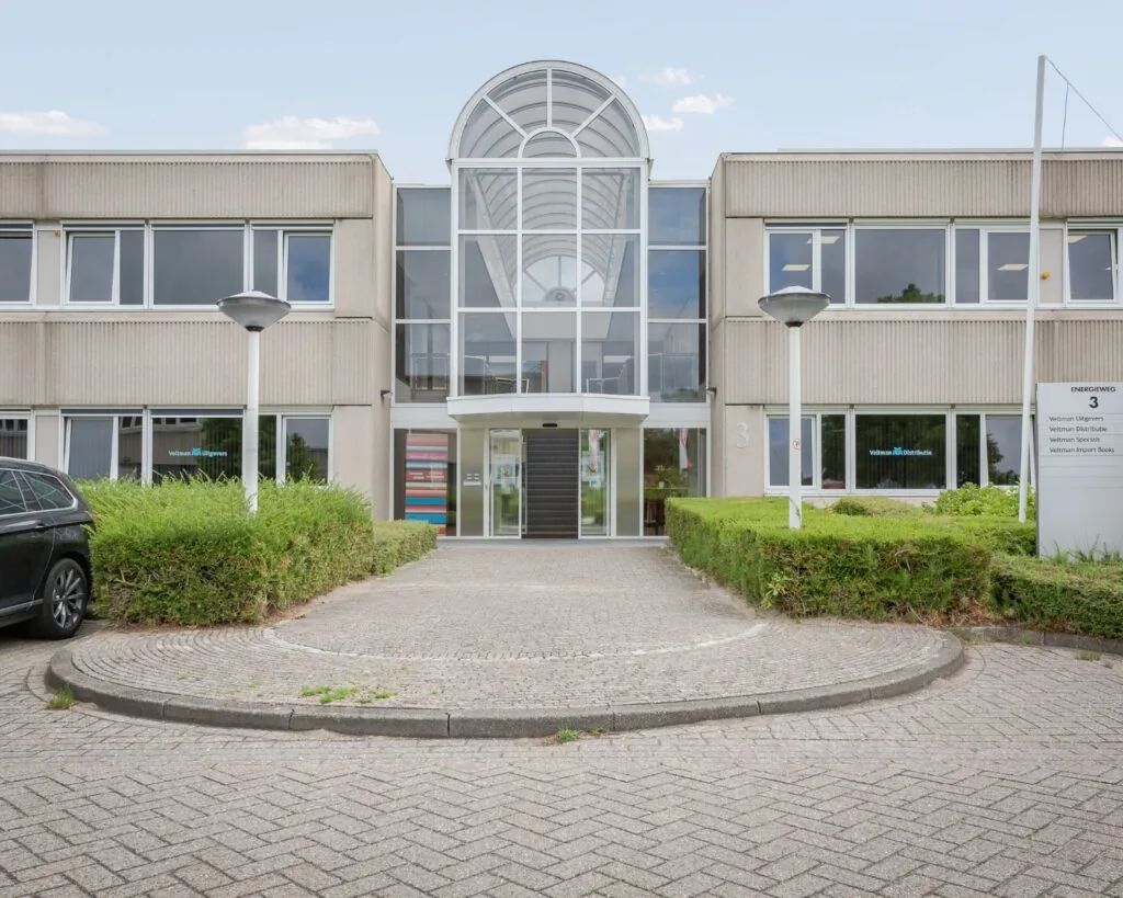Vooraanzicht van een modern kantoorgebouw aan de Energieweg 3, met glazen entree en bord met bedrijfsnamen van Veltman Uitgevers.