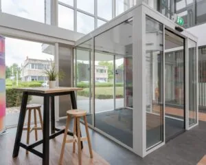 Entreehal met glazen draaideur en een hoge tafel met krukken en een plant.