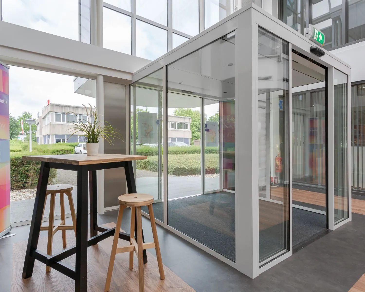 Entreehal met glazen draaideur en een hoge tafel met krukken en een plant.