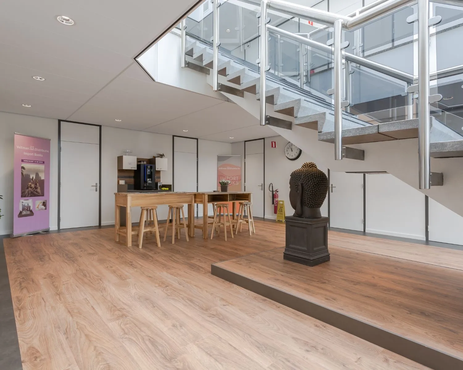 Moderne kantoorruimte met houten vloer, een zitgedeelte, een koffieautomaat en een trap met glazen balustrade.