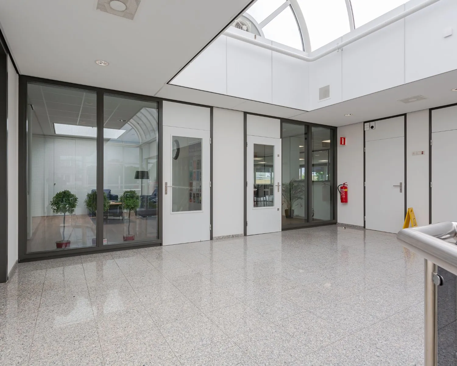 Lichte, moderne kantoorruimte met glazen wanden, binnendeuren en een marmeren vloer.