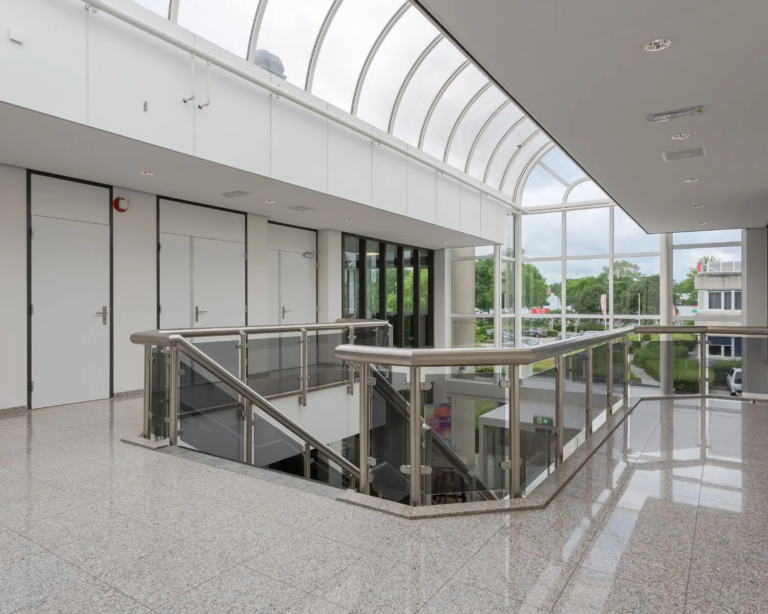 Moderne en lichte kantoorgebouwhal met glazen dak en trap naar beneden.