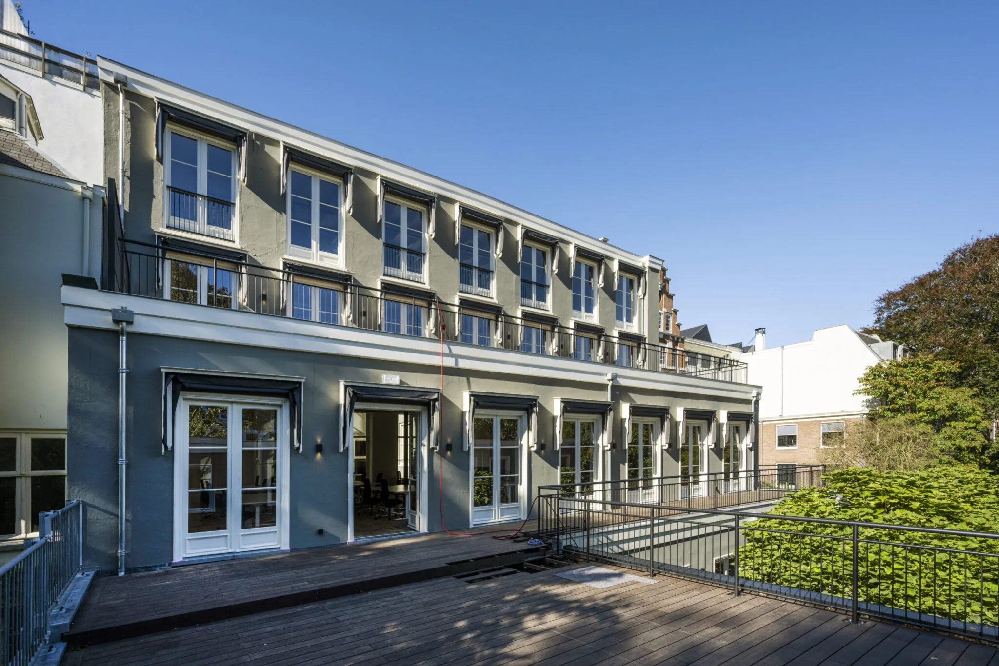 Achterzijde van een modern gerenoveerd pand met grote ramen en een houten terras.