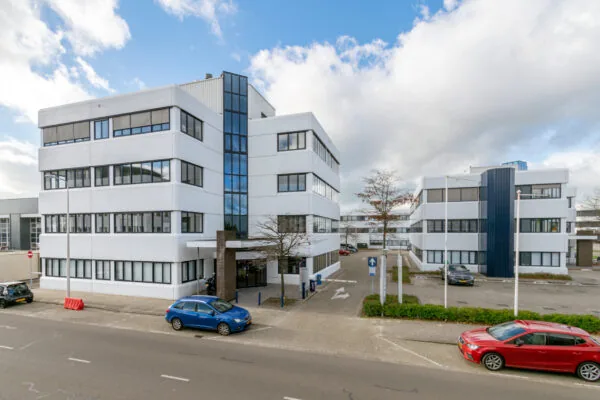 Wit kantoorgebouw aan de Atoomweg 400 met parkeerplaatsen en auto's op de voorgrond.