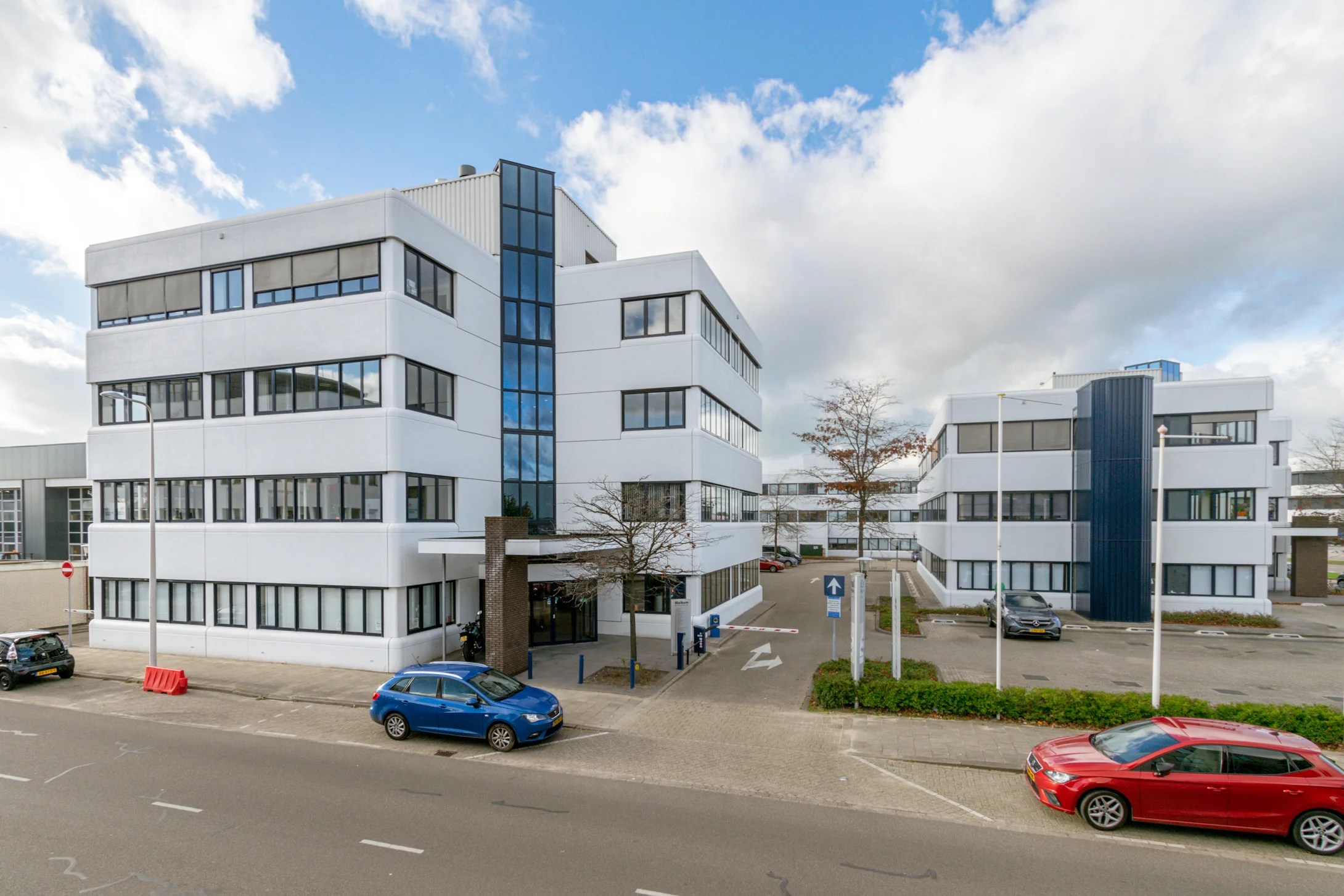 Wit kantoorgebouw aan de Atoomweg 400 met parkeerplaatsen en auto's op de voorgrond.