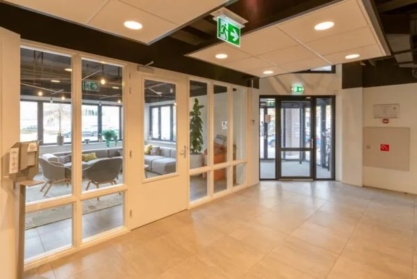 Ingang en ontvangsthal van een modern kantoorpand aan de Atoomweg, met zicht op een wachtruimte en glazen deuren.