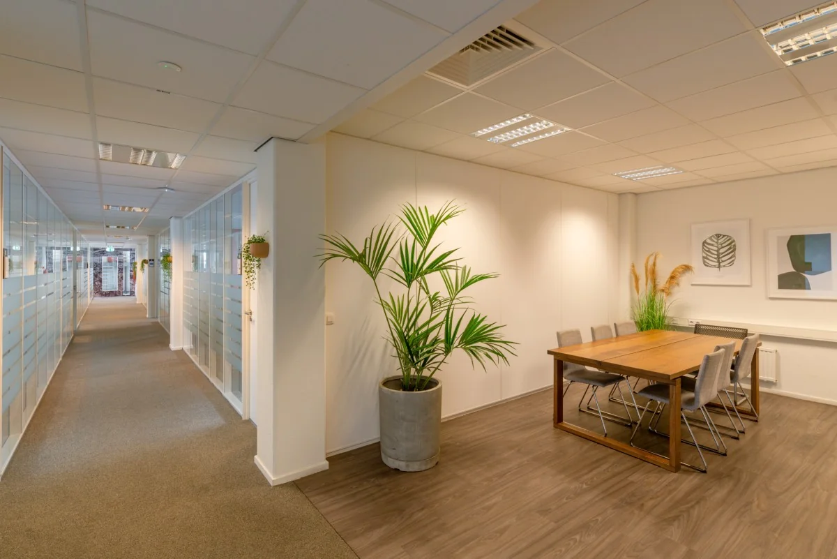 Vergaderruimte met houten tafel, zes stoelen en planten, gelegen aan een glazen kantoorhal in Atoomweg 400.