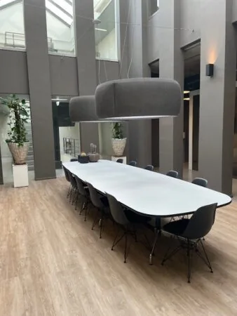 Modern atrium met een lange vergadertafel, stijlvolle stoelen en hanglampen onder een glazen dak.