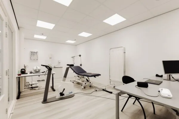Moderne behandelkamer in Badhoevedorp met fitnessapparatuur, onderzoeksbank en werktafel met computer.