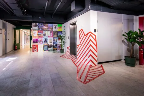 Hal met lift, kleurrijke posters aan de muur en opvallende rood-witte lijnen bij de Bernadottelaan.