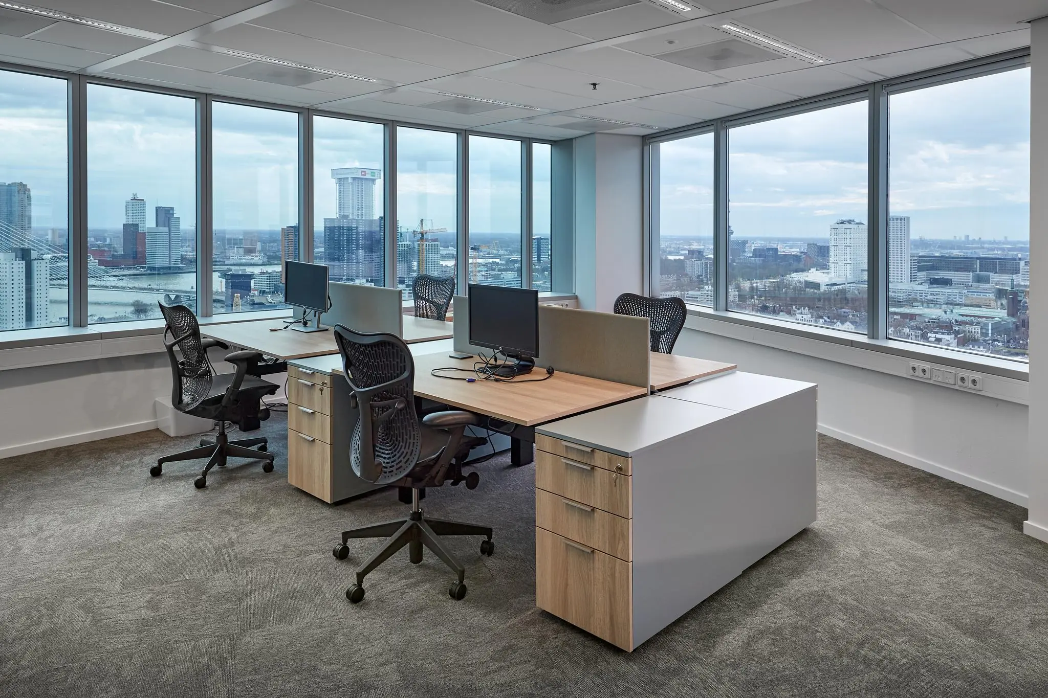 Modern kantoorinterieur met vier werkplekken en uitzicht op de Rotterdamse skyline vanaf Blaak 555.