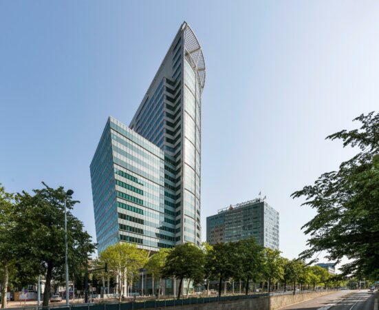 Hoog gebouw Blaak 555 in Rotterdam met moderne glazen gevel, omringd door bomen en stadsverkeer.