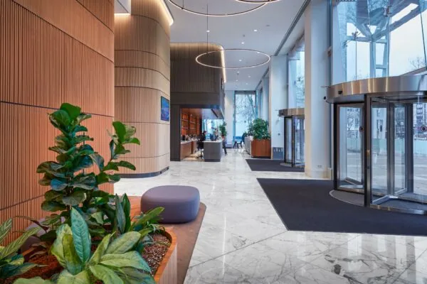 Moderne en lichte entreehal van Blaak 555 met marmeren vloer, houten wandafwerking en groene planten.