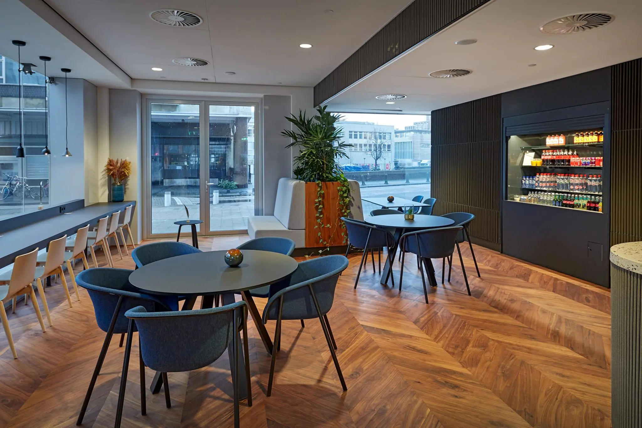 Moderne kantine in Blaak 555 met zitplaatsen, planten, een gekoelde drankautomaat en grote ramen met uitzicht op de stad.