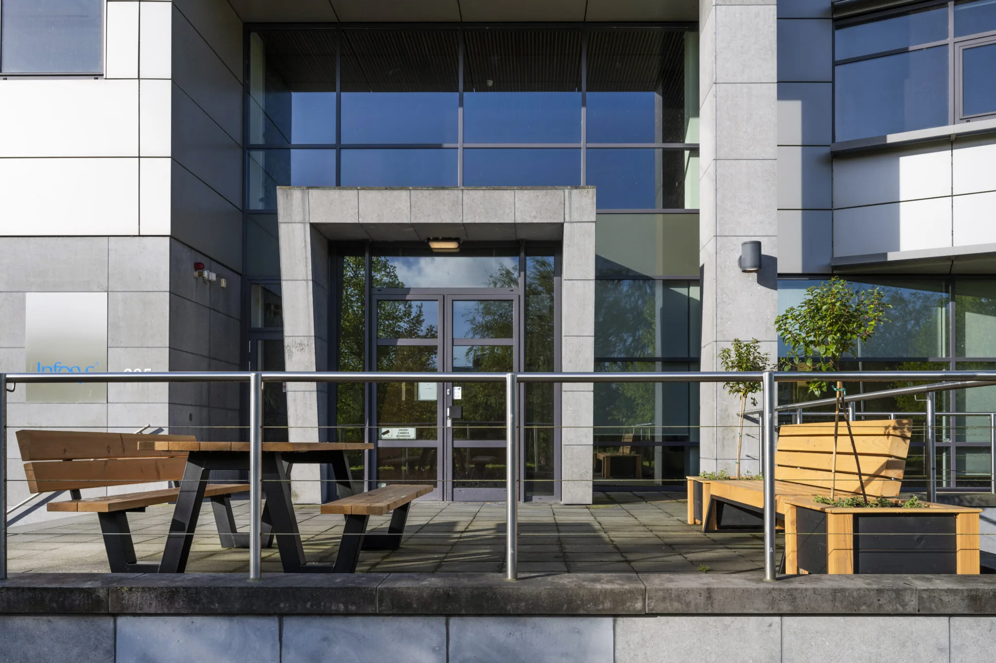 Vooraanzicht van een modern kantoorgebouw aan Boeing Avenue 015 met houten zitbanken en planten op het terras.