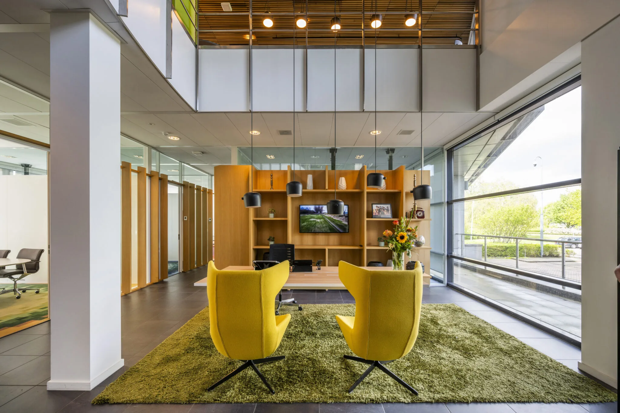 Moderne kantoorlounge aan de Boeingavenue met gele stoelen, groene vloerkleed en een houten wandmeubel, ontworpen door Paul Starink.