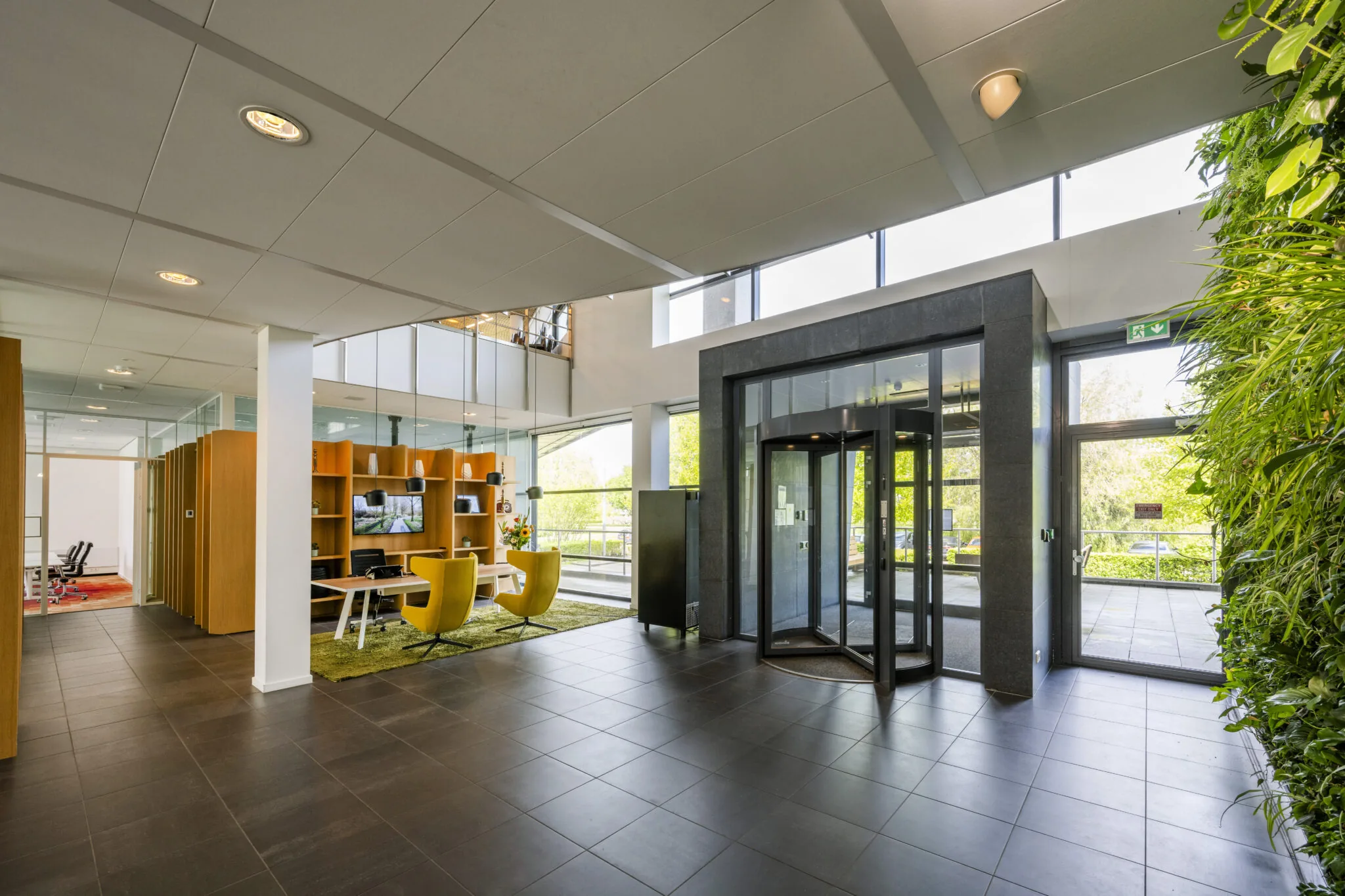 Moderne, lichte kantoorlobby aan de Boeingavenue met een draaideur, groene plantenwand en zithoek met geel meubilair.