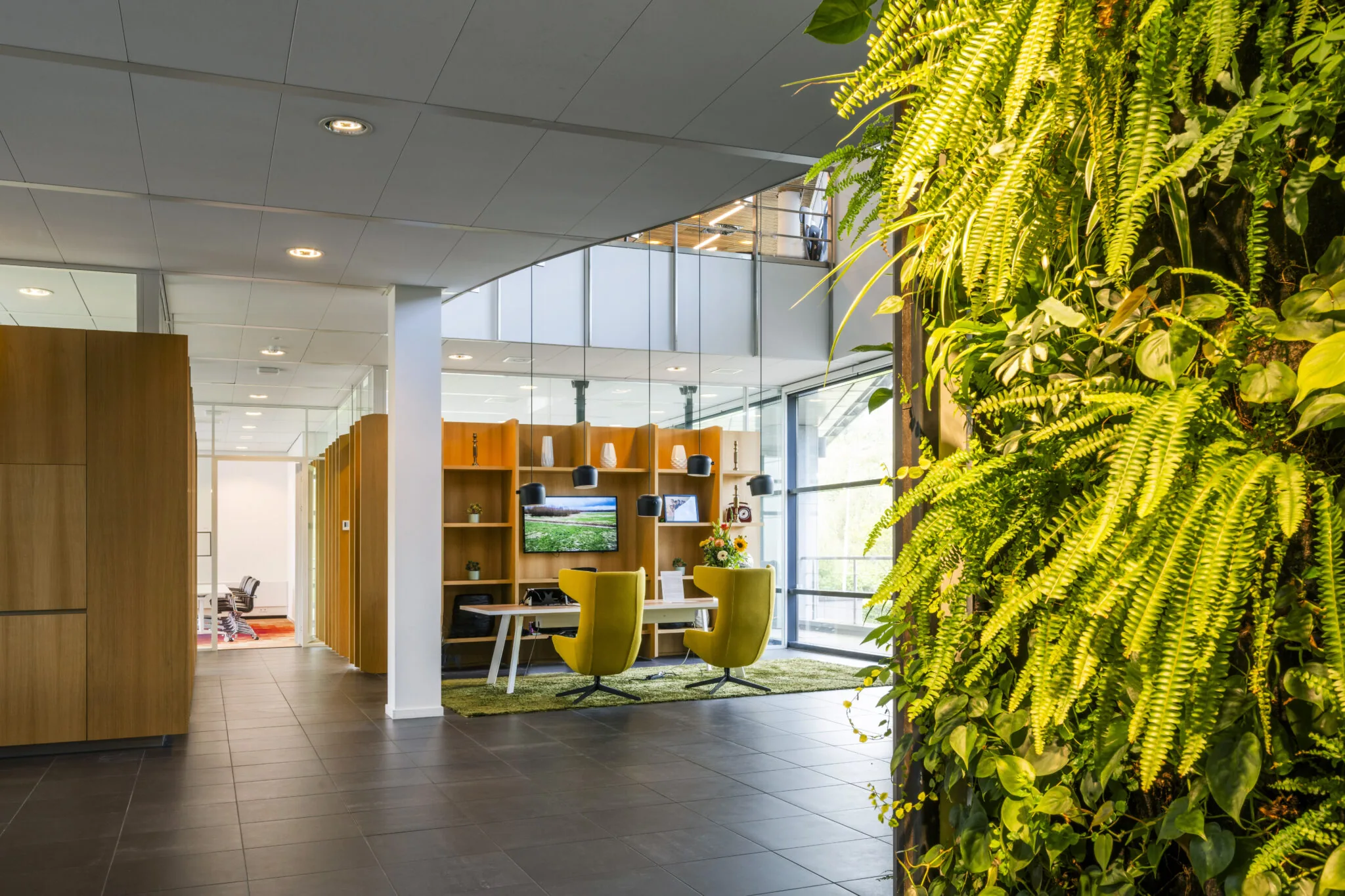 Modern kantoorinterieur aan de Boeingavenue met groene plantenwand, houten meubilair en zitruimte met gele stoelen.