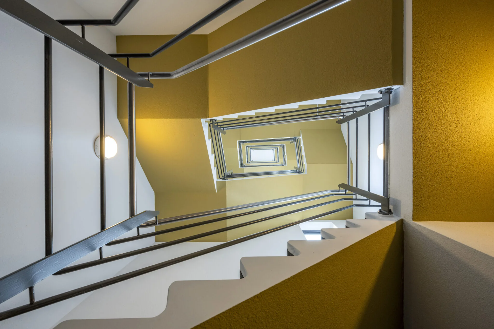 Blik omhoog in trappenhuis met gele muren en metalen leuningen in Boeingavenue 040, gefotografeerd door Paul Starink.