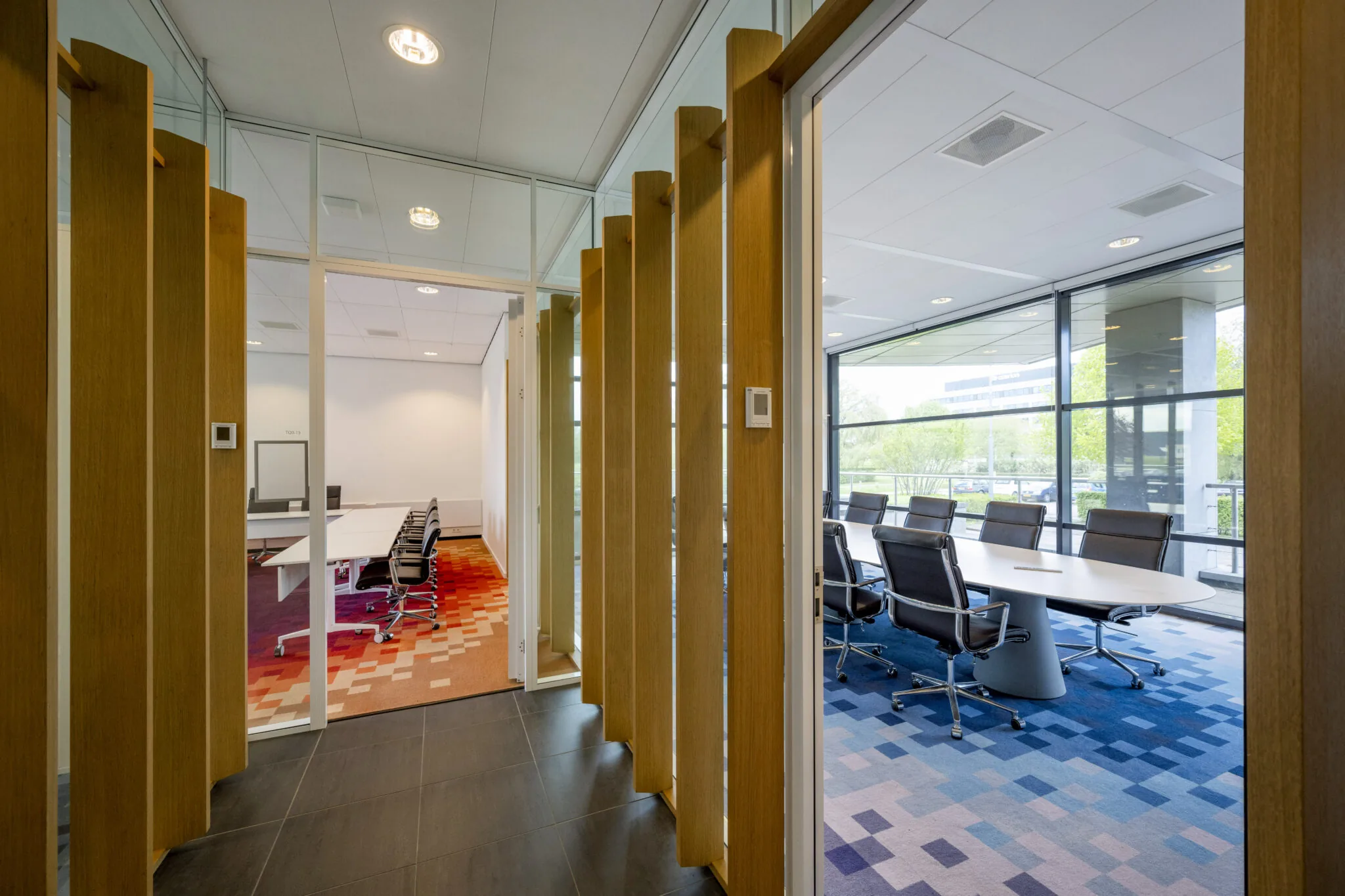 Twee moderne vergaderruimtes aan Boeing Avenue met glazen wanden, kleurrijke vloerbedekking en uitzicht op groen.