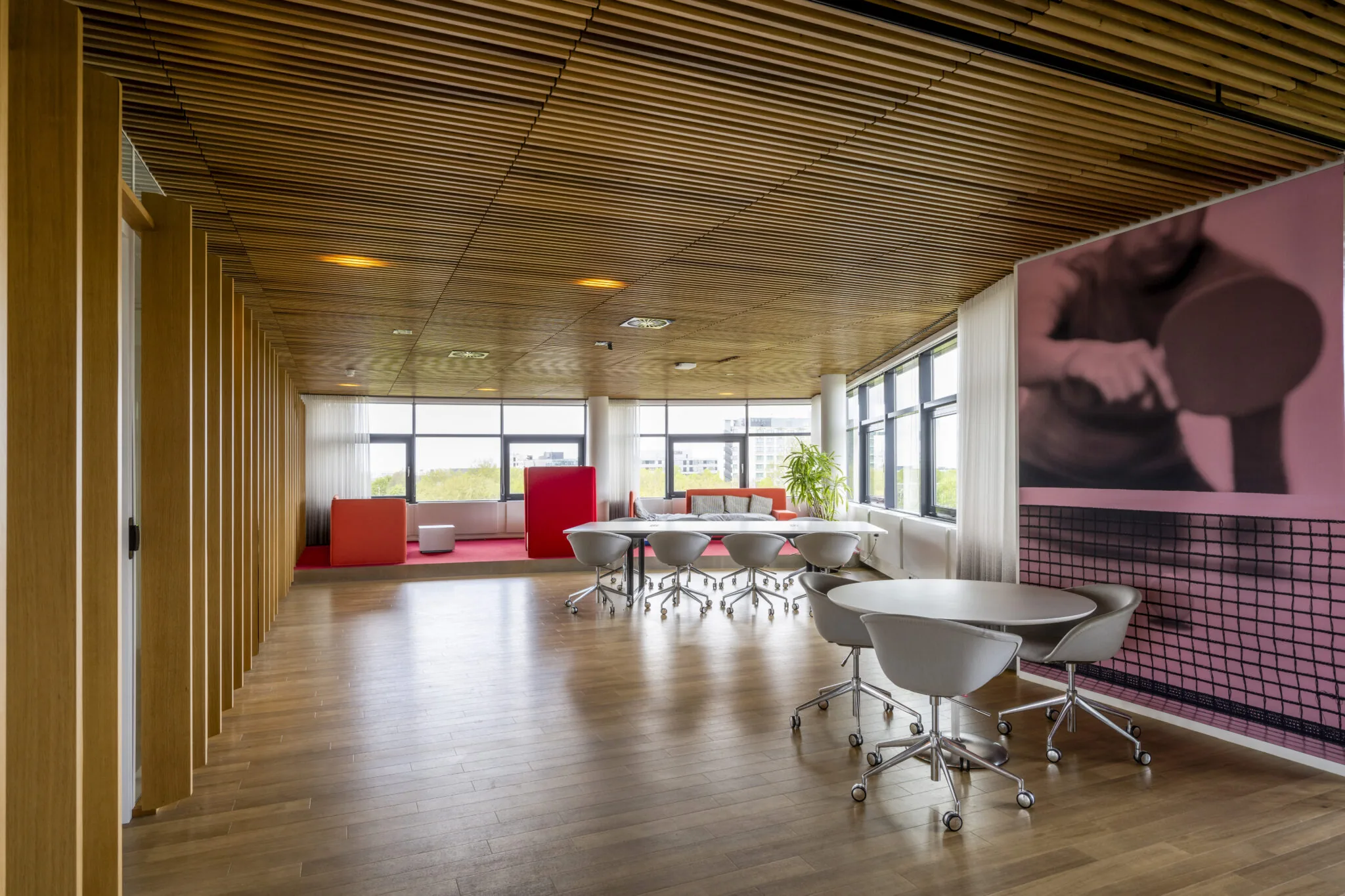 Moderne kantoorruimte aan de Boeingavenue met houten plafond, flexwerkplekken en een grote muurfoto van een tafeltennisspeler.