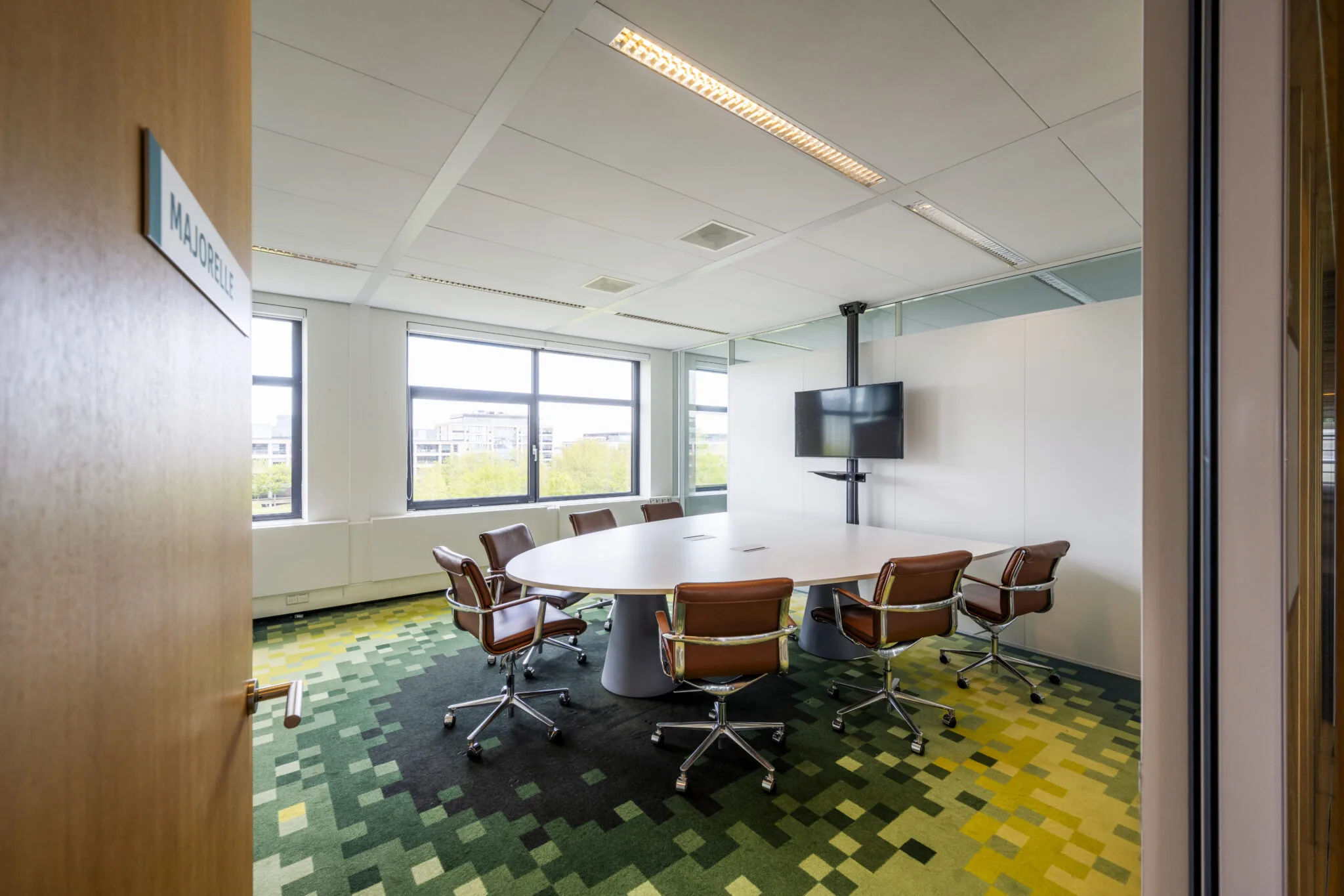 Vergaderruimte 'Majorelle' met ovale tafel, acht bruine stoelen en een scherm aan de muur in een modern kantoor aan de Boeing Avenue.
