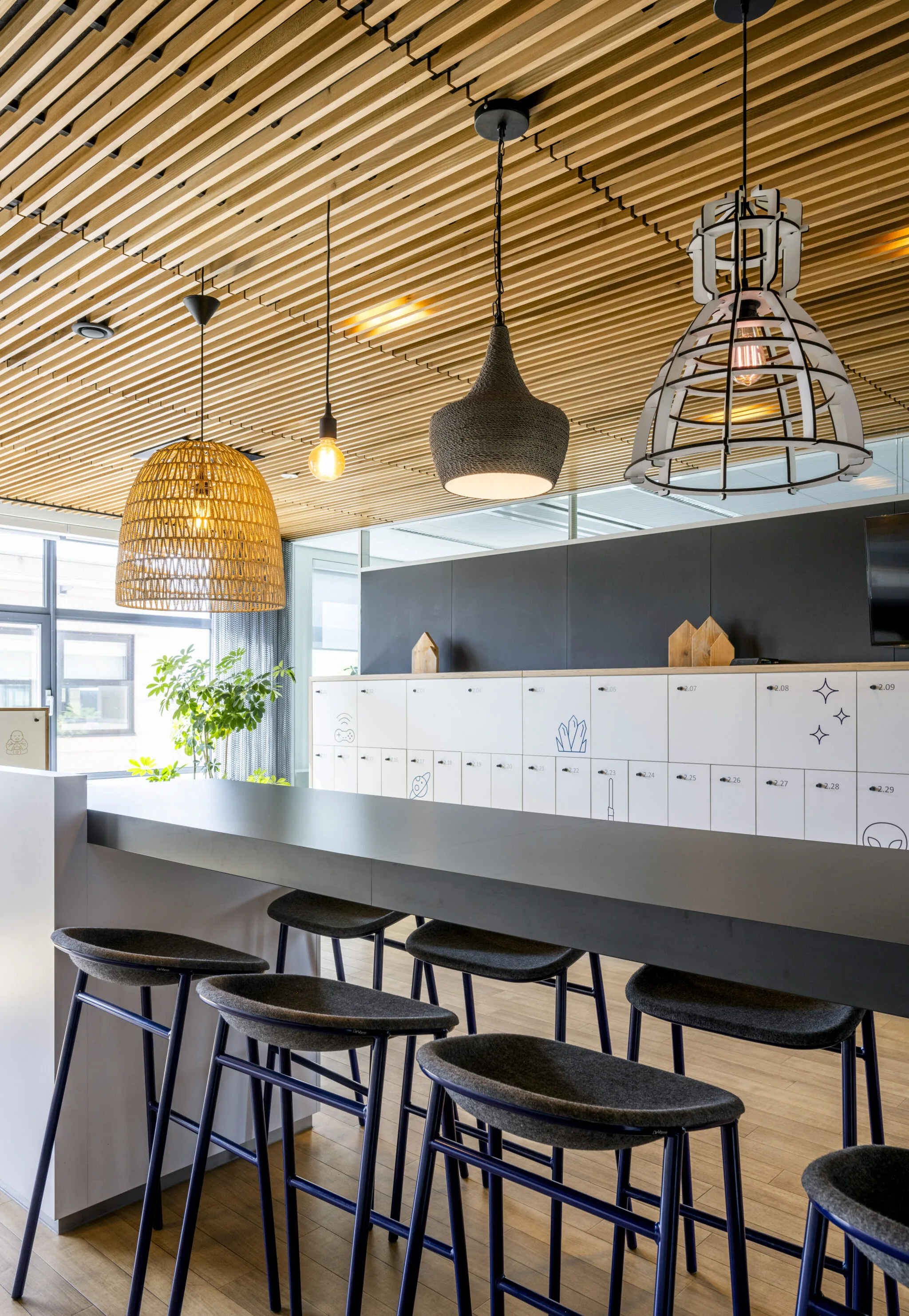 Moderne kantoorkeuken met hoge zitplaatsen, opvallende hanglampen en een wand met afsluitbare lockers bij Boeing Avenue, gefotografeerd door Paul Starink.