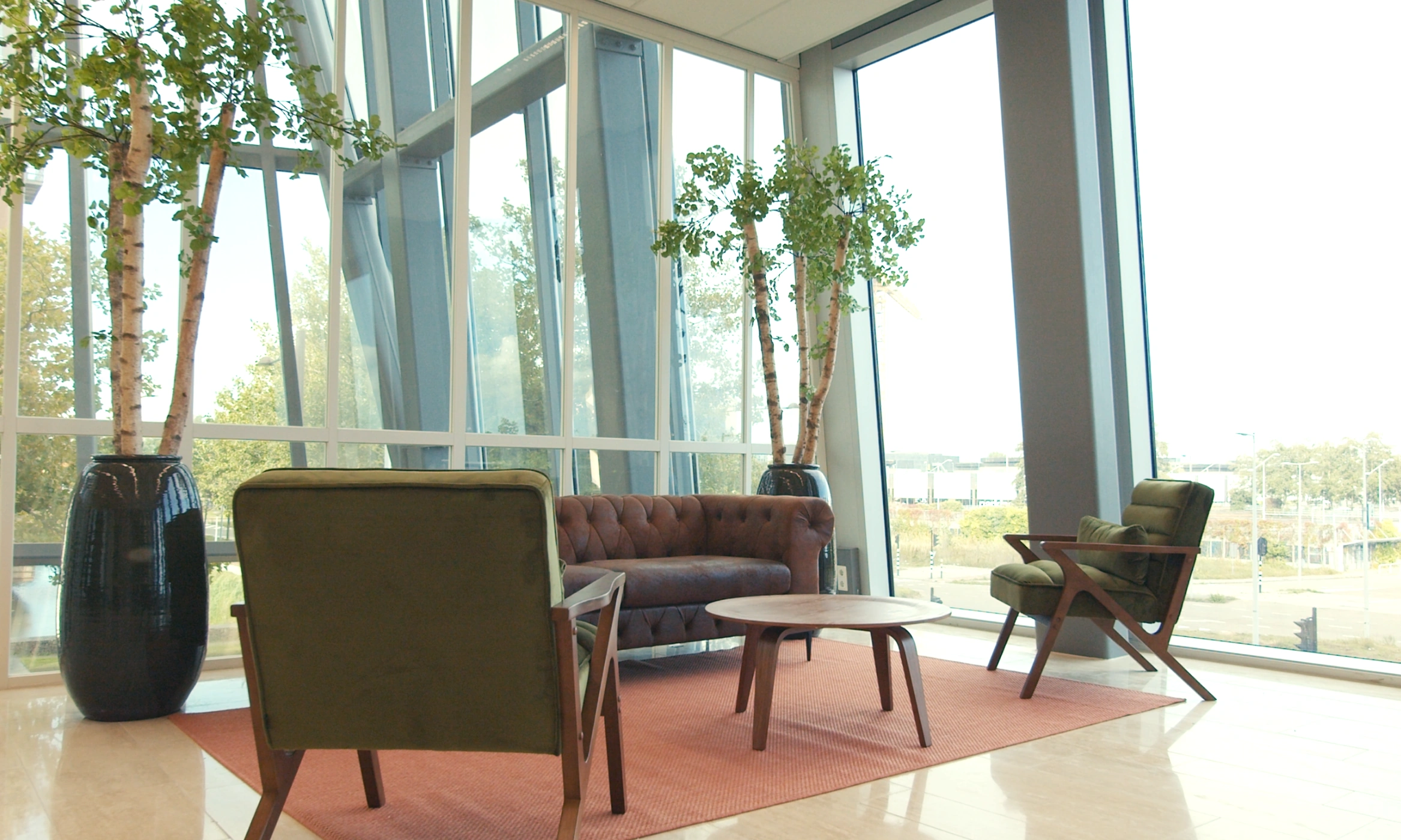 Moderne wachtruimte in Centrale Hart3 met groene stoelen, een bruine bank, houten tafel en grote kamerplanten bij hoge ramen.