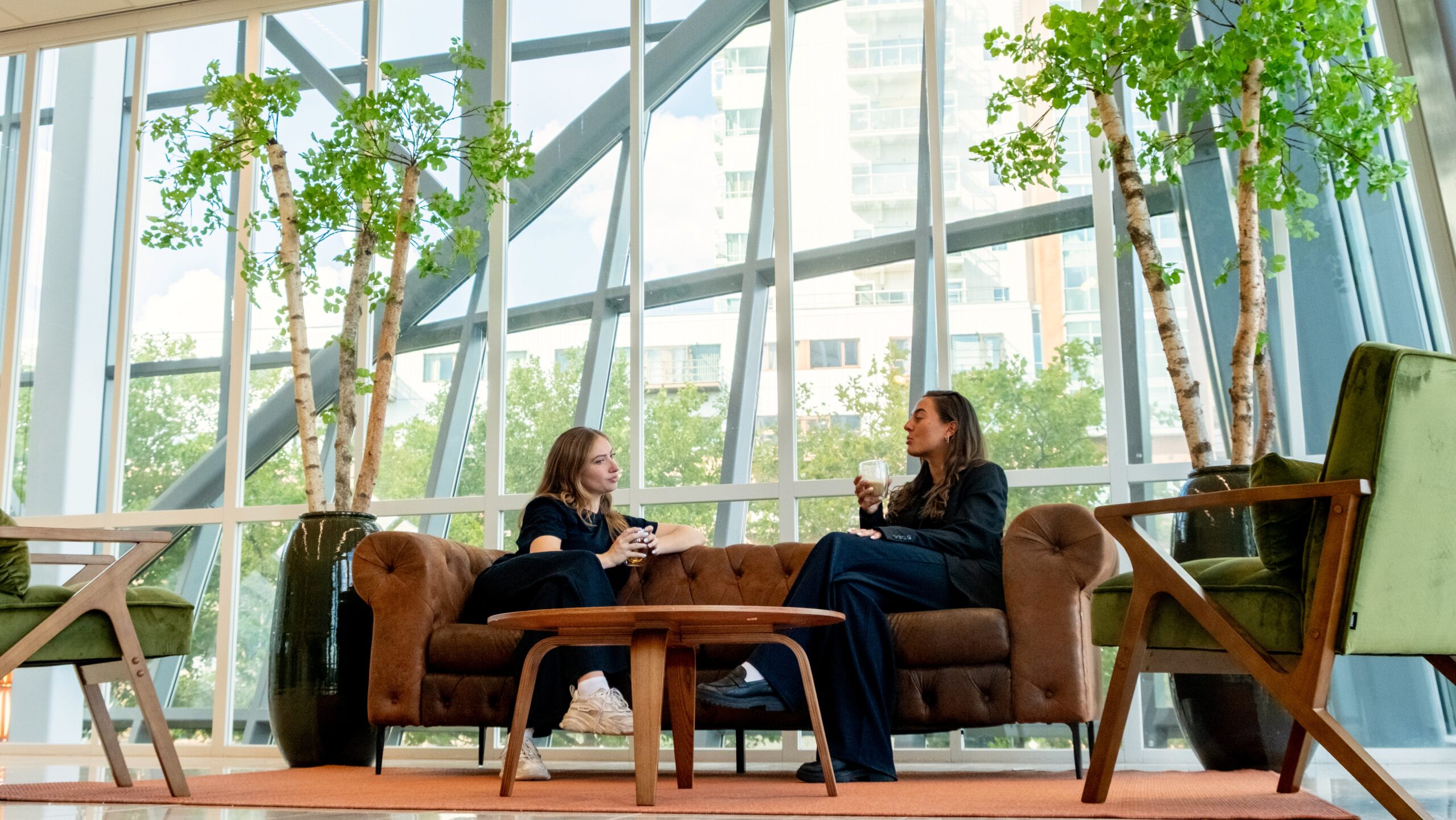 Twee vrouwen zitten ontspannen op een bank in het gebouw Centrale Hart7 en drinken koffie.