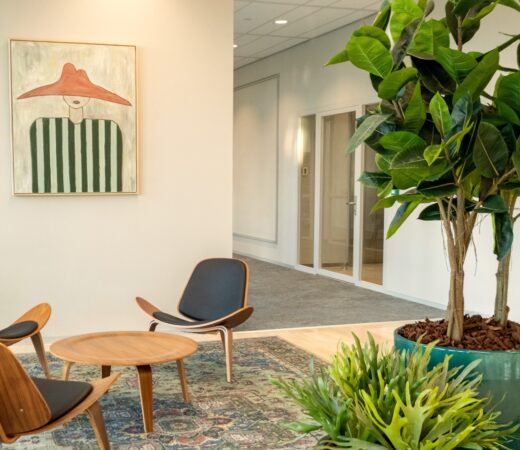 Moderne wachtruimte in Centrale Hart9 met houten stoelen, een ronde tafel, grote kamerplant en schilderij aan de muur.