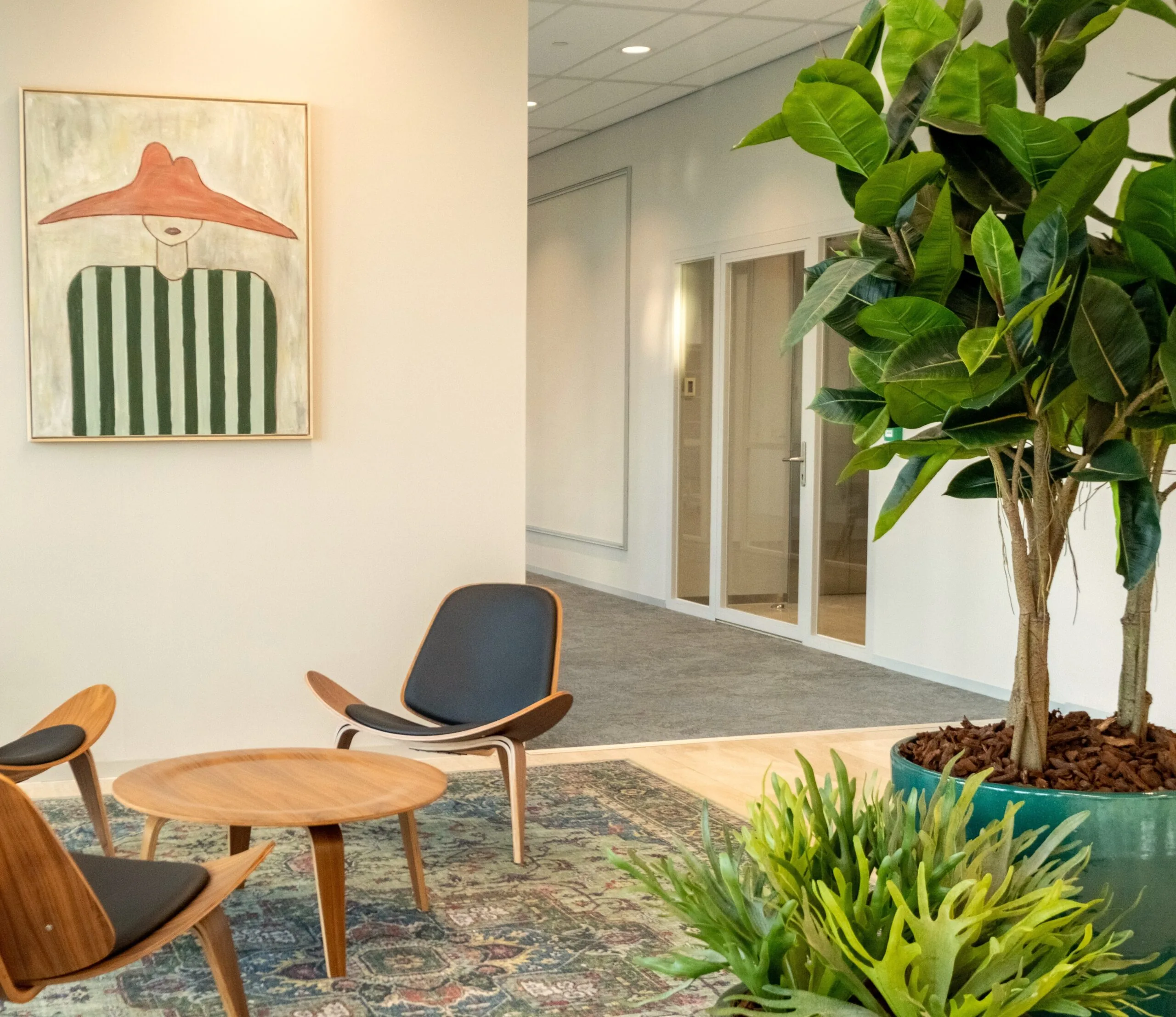 Moderne wachtruimte in Centrale Hart9 met houten stoelen, een ronde tafel, grote kamerplant en schilderij aan de muur.