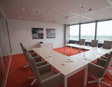 Vergaderruimte met U-vormige opstelling, moderne stoelen, schrijfmateriaal en uitzicht op de stad.