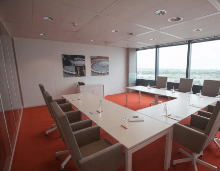 Vergaderruimte met U-vormige opstelling, moderne stoelen, schrijfmateriaal en uitzicht op de stad.