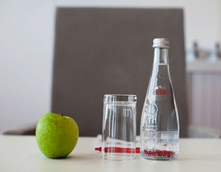 Een groene appel, een omgekeerd glas en een fles Evian-water staan op een tafel.