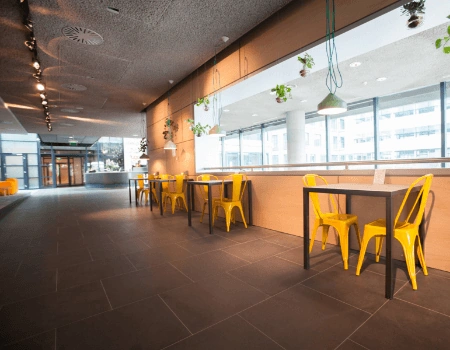 Moderne, lichte zitruimte met gele metalen stoelen en hoge ramen in een kantoorgebouw.