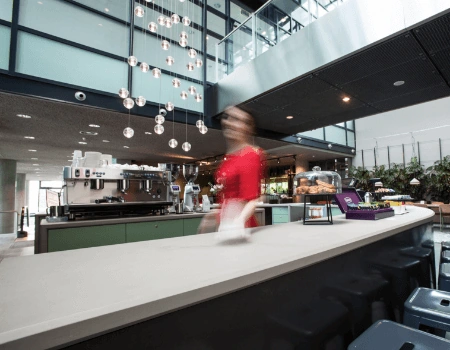 Moderne koffiebar met een onscherp bewegende serveerster in een open en licht atrium.